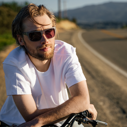 Man with sunglasses and a beard sitting on a bicycle in a scenic outdoor setting