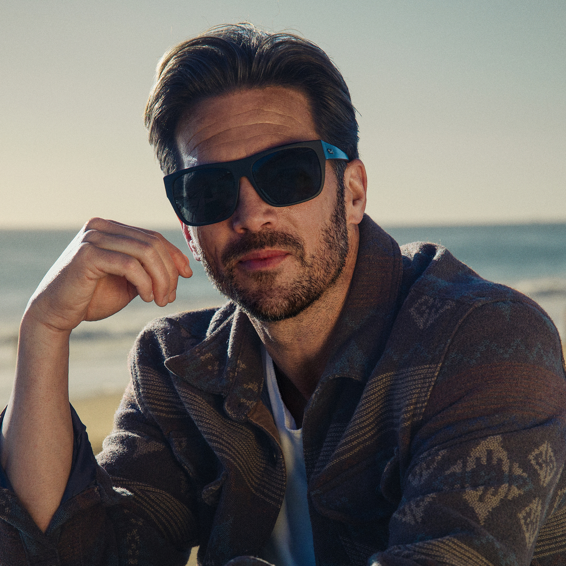 Man wearing sunglasses and a patterned jacket on a beach